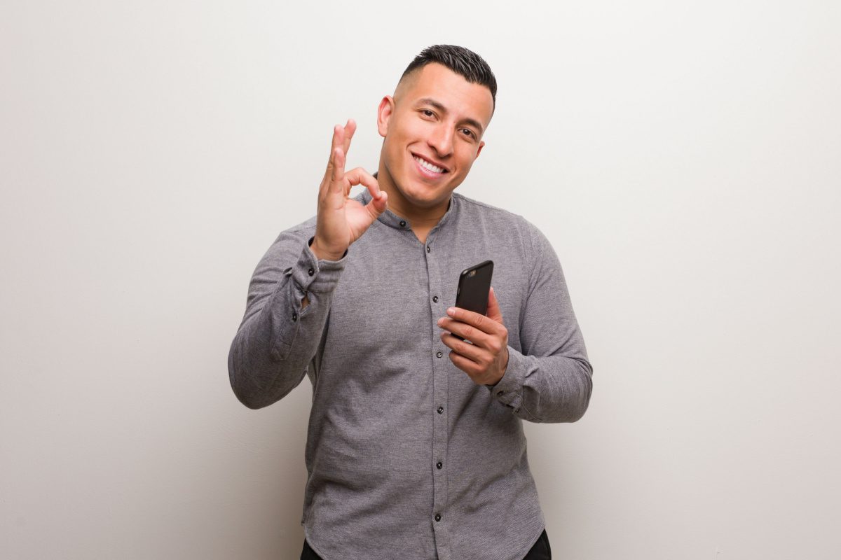 Photo of young professional man making the OK sign holding smart phone